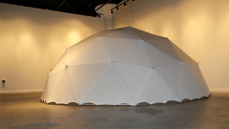 A large (14-foot wide) geodesic dome covered in white cloth sits on the floor of an art gallery.