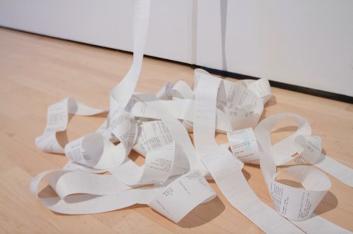 A pile of receipt paper sits on a wooden gallery floor.